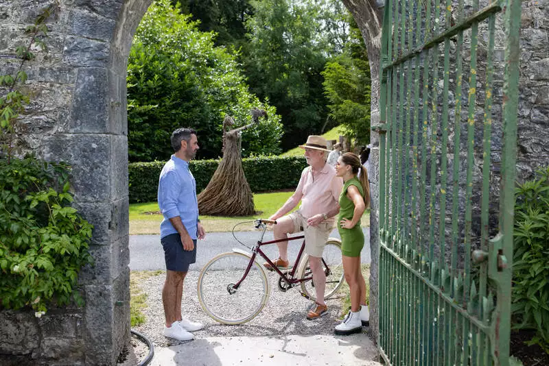 Destination wedding in Ireland at Adare Manor, County Limerick — bride and groom outdoors on the castle grounds conversing with a guest on a bicycle.