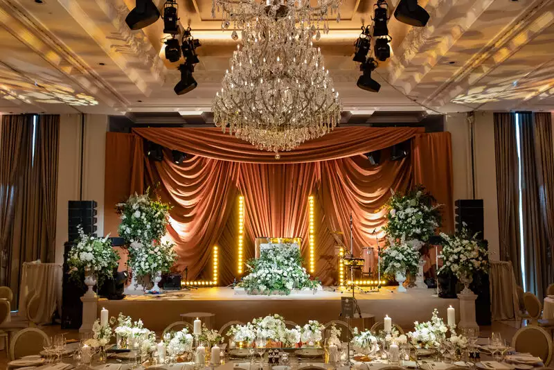 Destination wedding in Ireland at Adare Manor, County Limerick — wedding dinner stage designed with white floral arrangements and greenery, rich gold draping backdrop, and chandelier overhead.