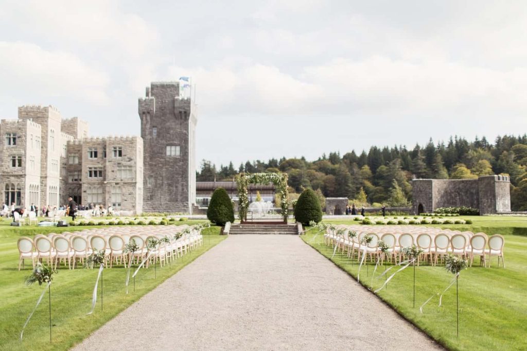 Irish castle wedding at Ashford Castle, County Mayo — outdoor ceremony setup on the estate grounds with chairs arranged along a central aisle leading to a wooden ceremony structure.