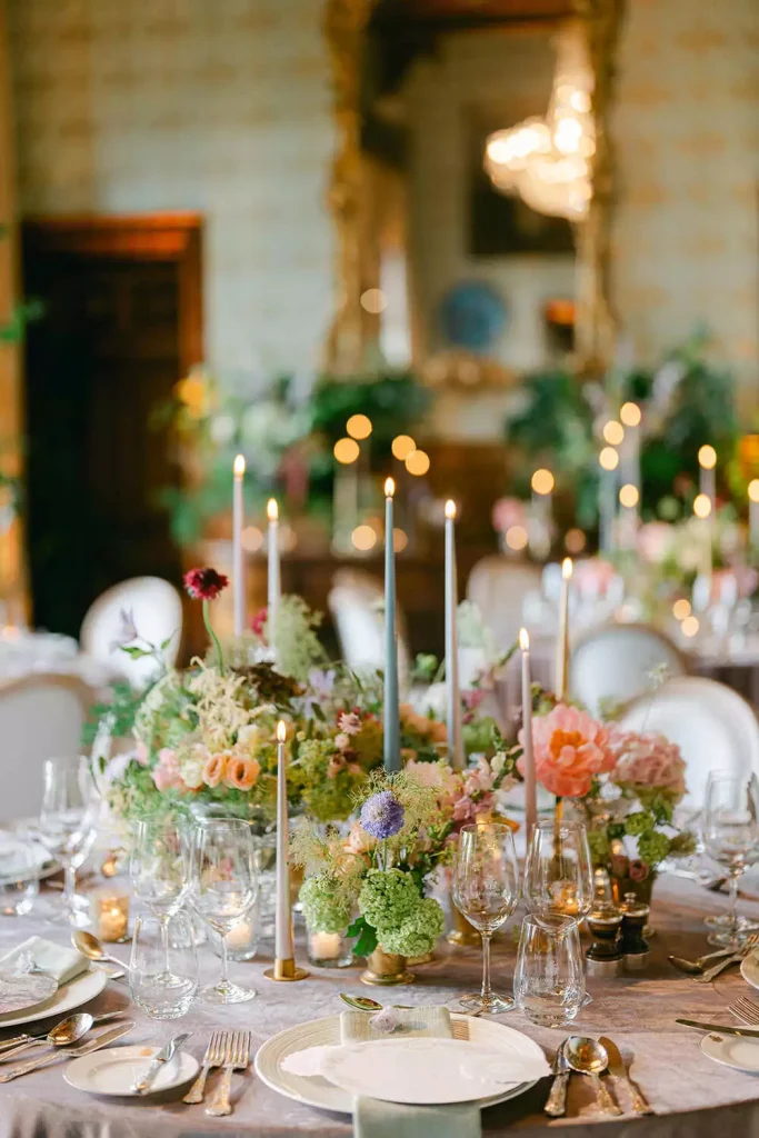 Elegant banquet table with pastel flowers, tall candles, and neatly set plates and glassware. - Informative: describes occasion setting and key elements (flowers, candles, tableware).