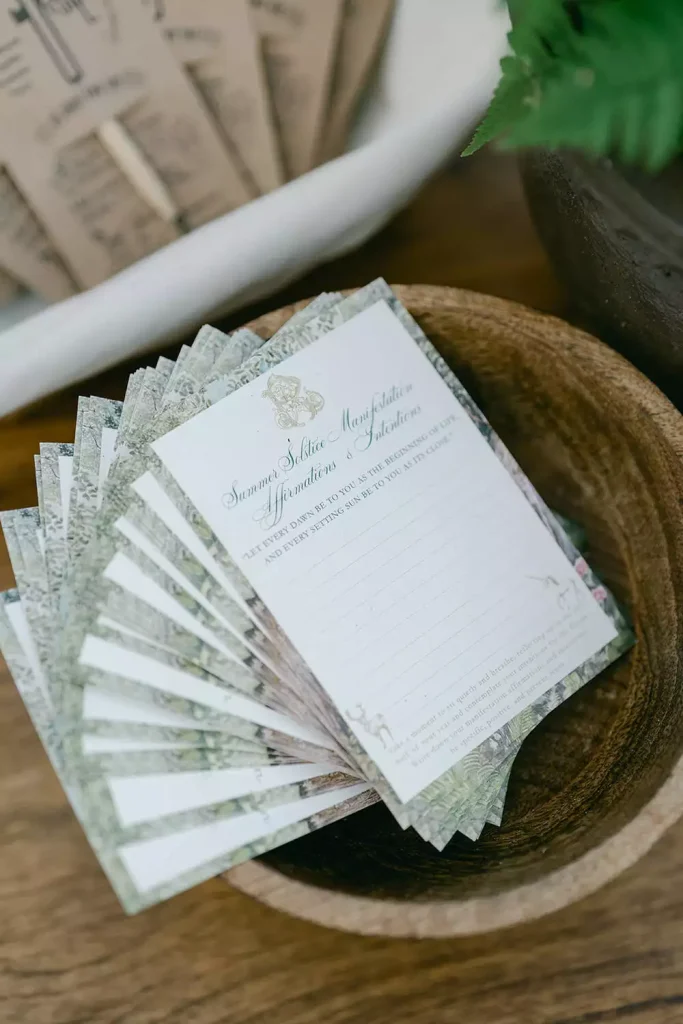Wedding invitation cards fanned out in a wooden bowl on a rustic surface with greenery nearby.