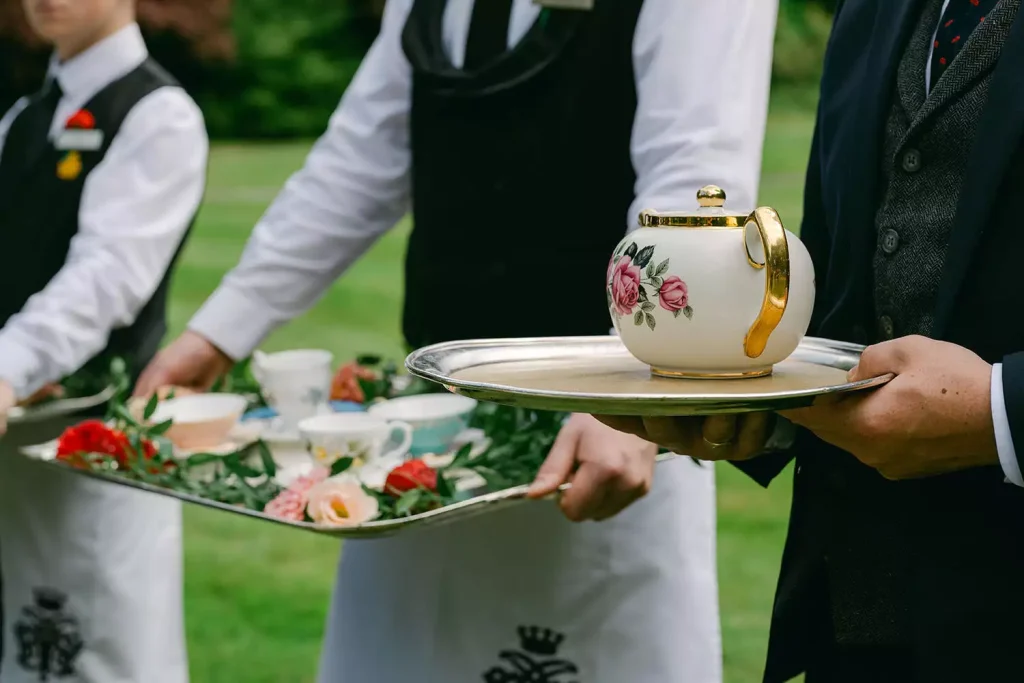 Destination wedding at Ashford Castle, County Mayo — wait staff lined up for tea service holding trays with a floral teapot and matching teacups.