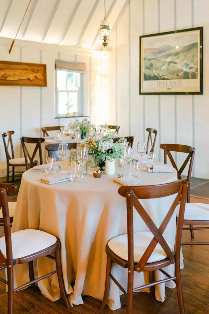 Destination wedding in Ireland at Ashford Castle, County Mayo — welcome party dining setup featuring a circular table surrounded by wooden chairs, set for dinner with a small floral arrangement at the centre.