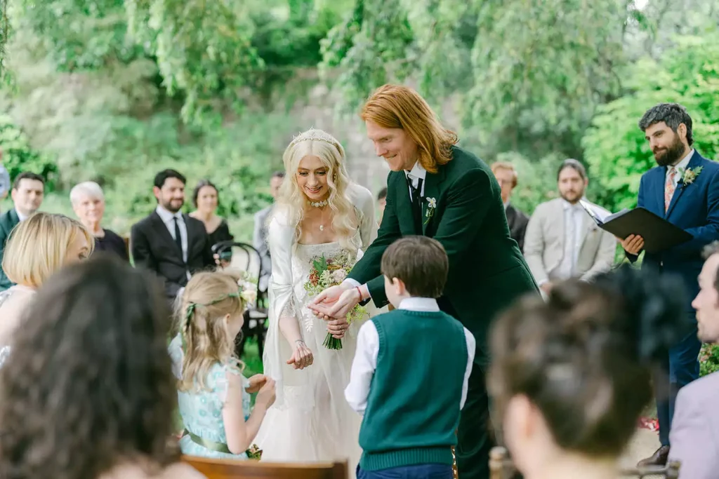Destination wedding in Ireland at Ashford Castle, County Mayo — bride and groom taking part in a ceremony ritual with two young children during an outdoor wedding ceremony.