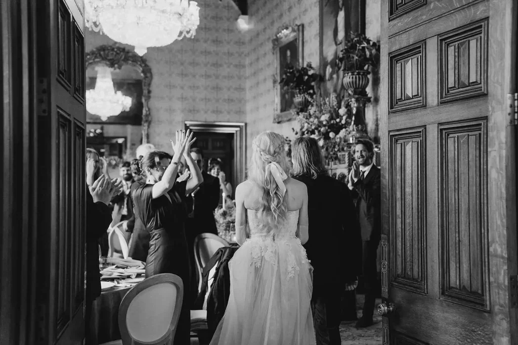 Destination wedding in Ireland at Ashford Castle, County Mayo — bride and groom making their entrance to the wedding dinner as guests stand and celebrate around the reception space.