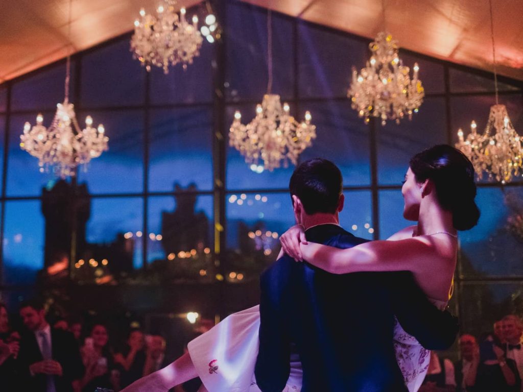 Irish castle wedding — bride and groom during a late-night marquee celebration, with the groom holding the bride beneath the illuminated structure.