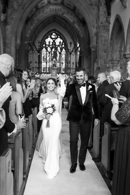 Irish destination wedding at Adare Manor, County Limerick — bride and groom holding hands during the church recessional, walking down the aisle as guests on either side clap and celebrate.