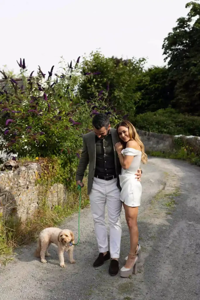 Irish destination wedding at Adare Manor, County Limerick — bride and groom outdoors during rehearsal dinner, with the groom holding their dog on a lead.
