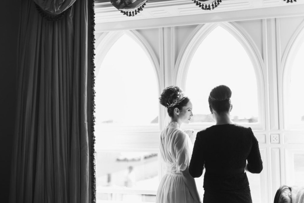 Irish destination wedding at Ashford Castle, County Mayo — bride and wedding planner standing in front of a large window during the morning wedding preparations.