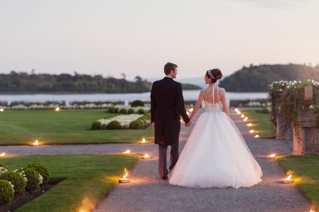 Irish destination wedding at Ashford Castle, County Mayo — bride and groom holding hands during an outdoor portrait overlooking Lough Corrib from the estate grounds.