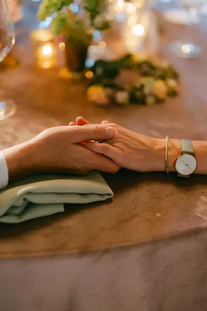 Irish destination wedding at Ashford Castle, County Mayo — two guests holding hands across the wedding dinner table, with a wristwatch visible on one guest beside the place settings.